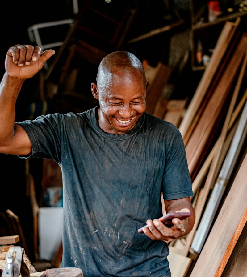 A carpenter in his workshop celebrating a message on his phone