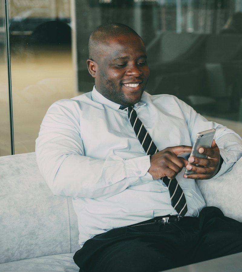 A man in a shirt and tie laughing as he looks at his phone